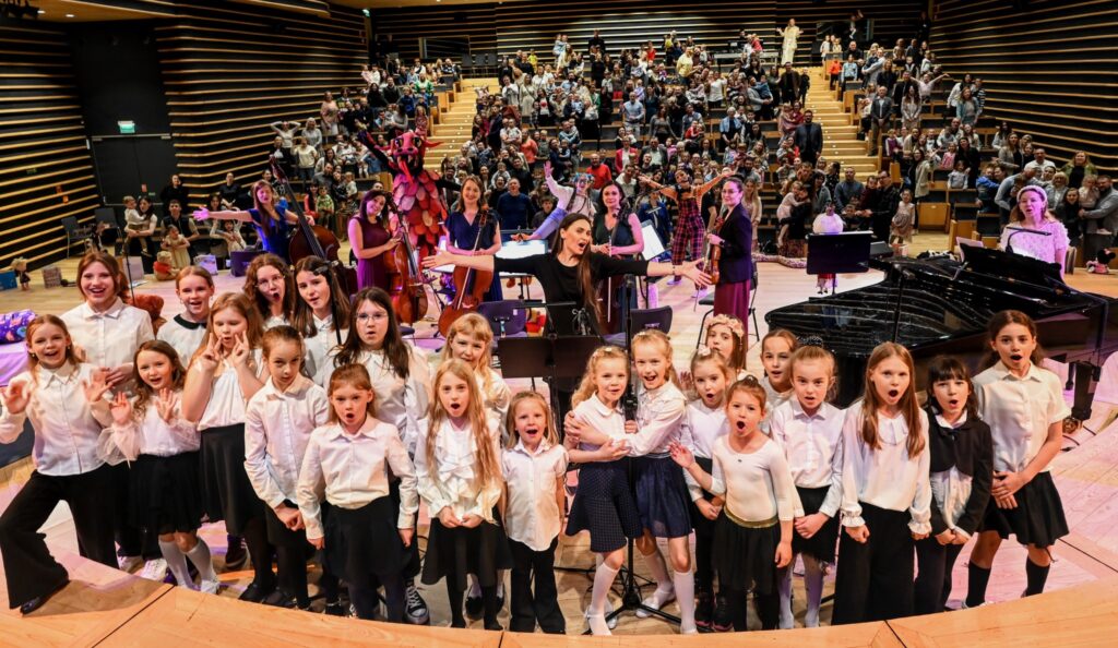 Grupa dzieci i muzyków na scenie podczas występu.