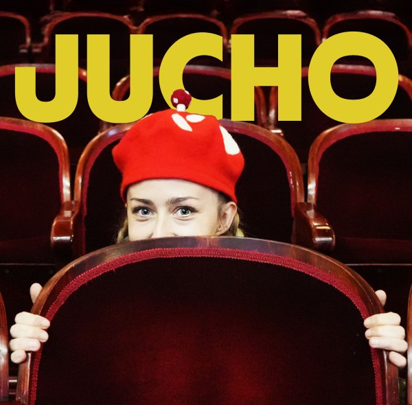 Osoba w czerwonej czapce patrzy zza oparcia fotela w teatrze.