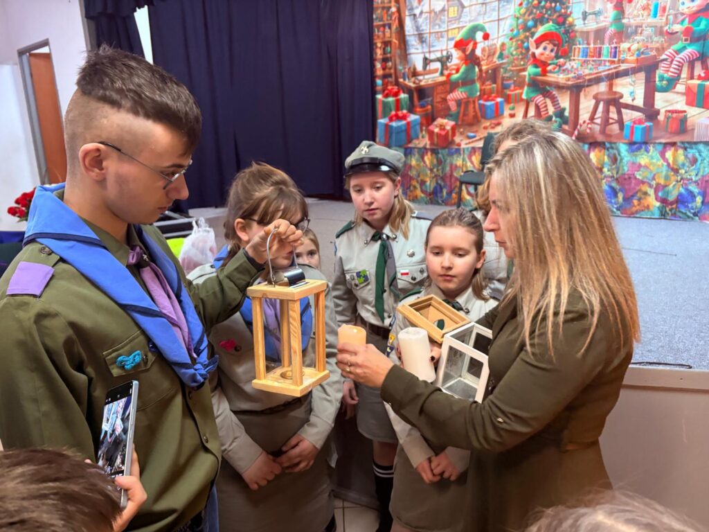 Grupa dzieci i dorosłych trzyma lanterny i świece.