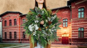 Kobieta trzyma wieniec przed czerwoną ceglaną budowlą.