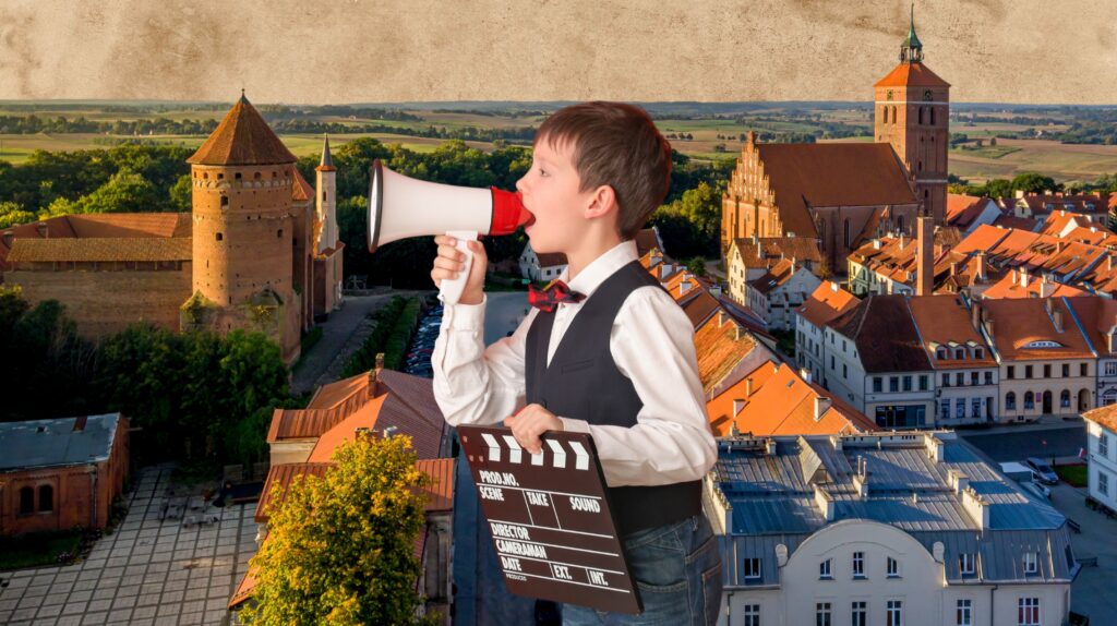 Chłopiec z megafonem i klapsami filmowymi na tle miasta.