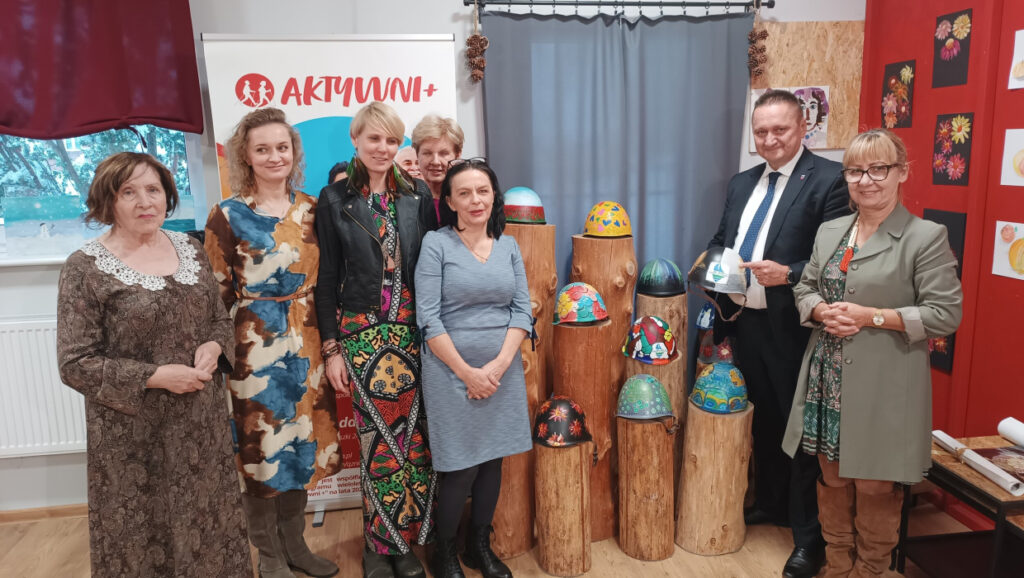 Grupa osób przy kolorowych dekoracjach stojących na drewnianych blokach.