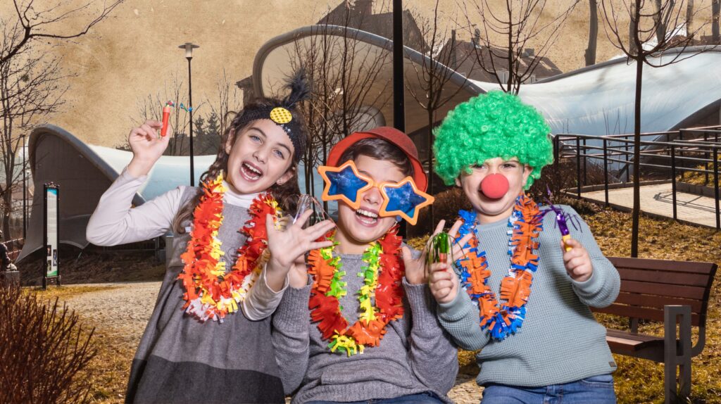 Trójka dzieci w kolorowych przebraniach na tle parku.