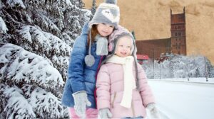 Dwie dziewczynki ubrane w zimowe kurtki stoją na śniegu.