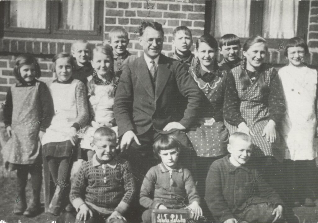 Grupa dzieci z nauczycielem na tle ceglanego budynku.