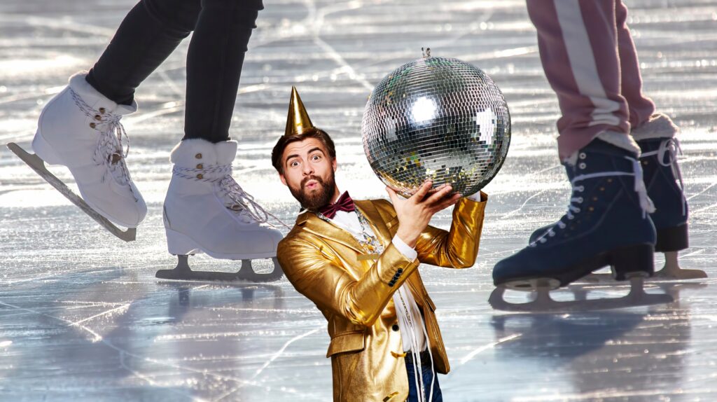 Mężczyzna w złotym garniturze trzyma dyskotekową kulę na lodowisku.