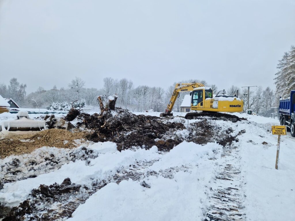Miejsce budowy z koparką w zimowym krajobrazie.