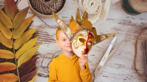 Dziecko trzyma maskę w kolorach złota i czerwieni.