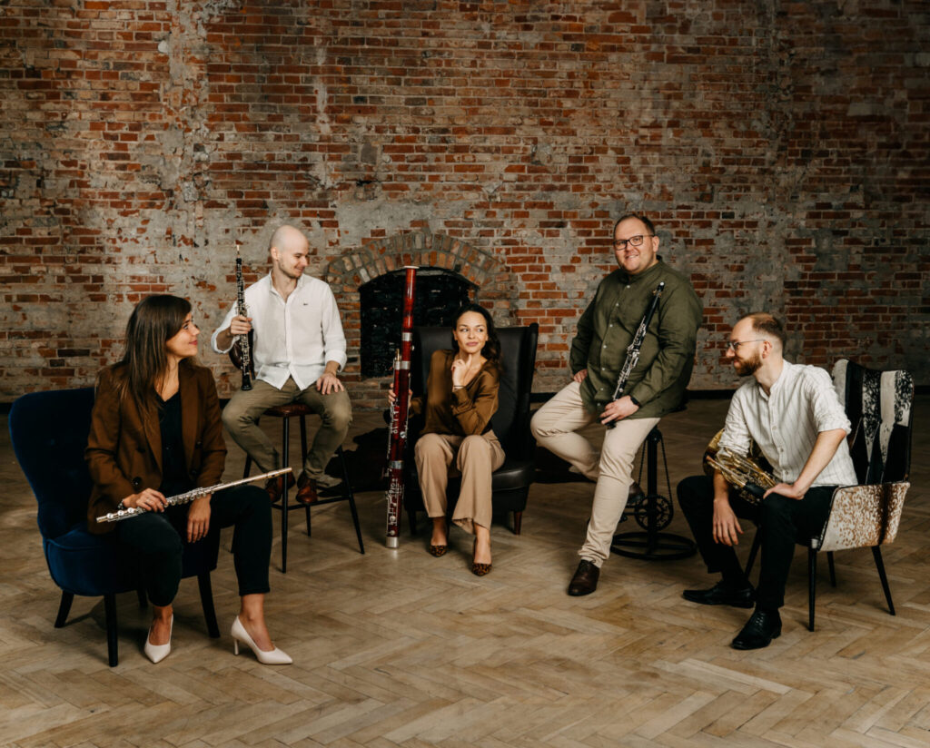 Grupa muzyków siedzących na krzesłach z instrumentami.