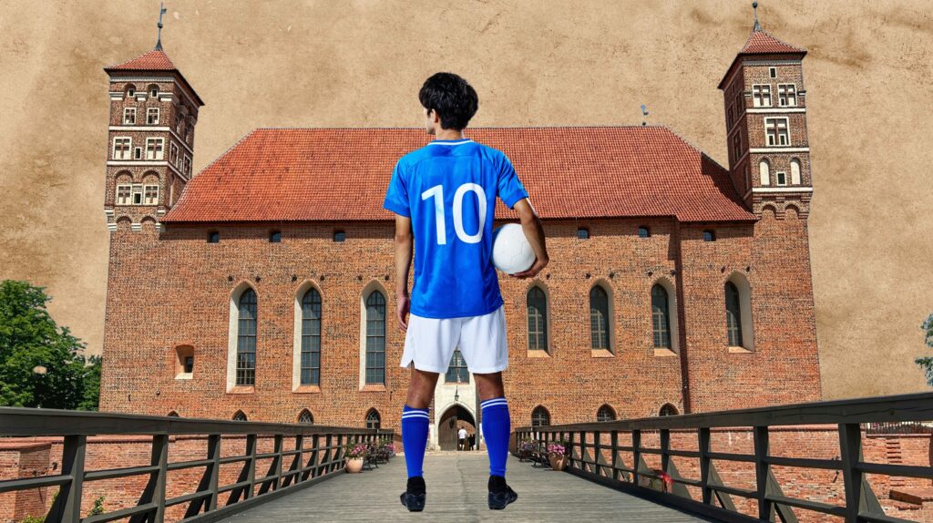 Młody piłkarz w niebieskiej koszulce z numerem 10 trzyma piłkę przed średniowiecznym zamkiem.