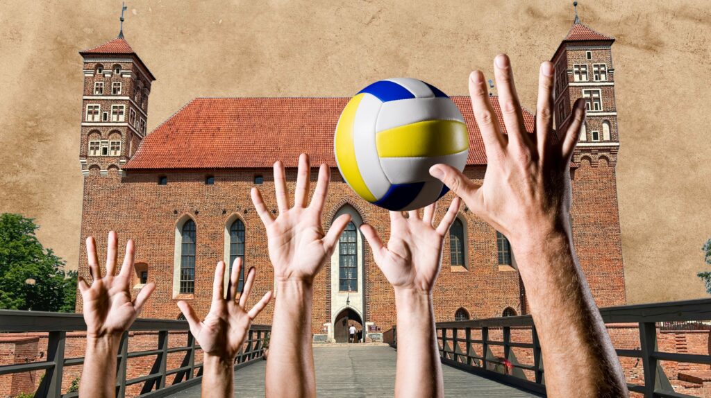 Ręce sięgające po piłkę siatkową przed budynkiem.