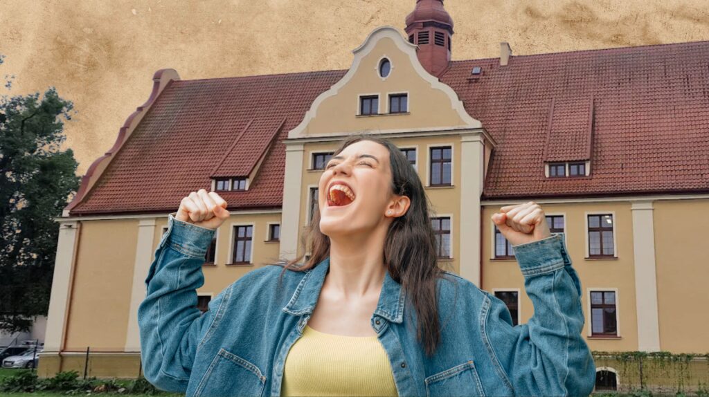 Uśmiechnięta kobieta w dżinsowej kurtce z piętrującym budynkiem w tle.