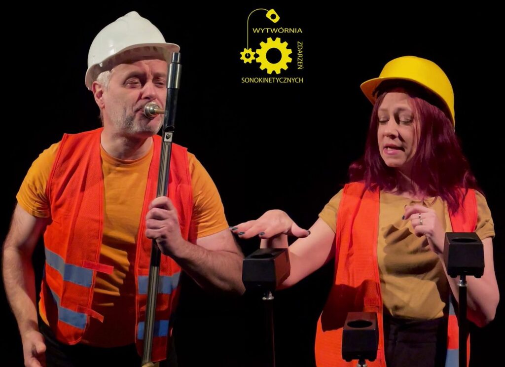 Dwójka artystów w kamizelkach odblaskowych i kaskach.