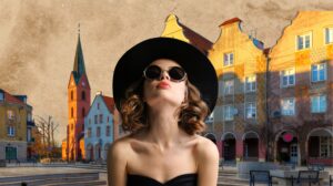 Kobieta w dużym kapeluszu i okularach przeciwsłonecznych na tle architektury.