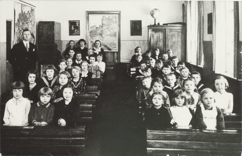 Uczniowie w szkolnej klasie z nauczycielem.