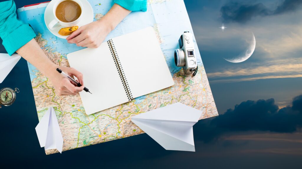 Osoba pisząca w notatniku na mapie z kubkiem kawy i aparatem fotograficznym.