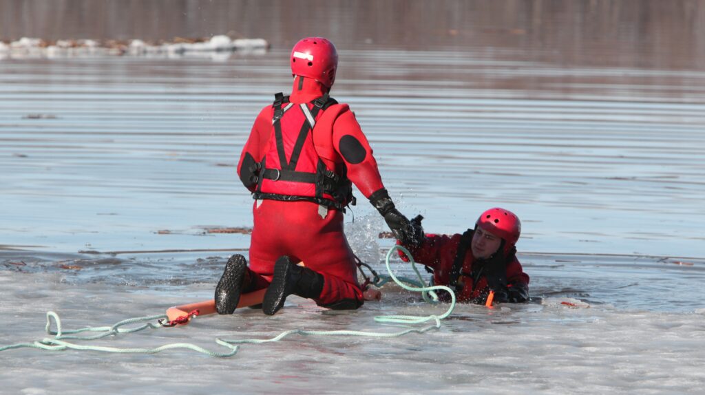 Ratownicy w czerwonych kombinezonach ratują osobę z wody.