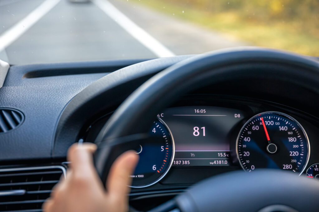 Widok z wnętrza samochodu przy kierownicy z prędkościomierzem.