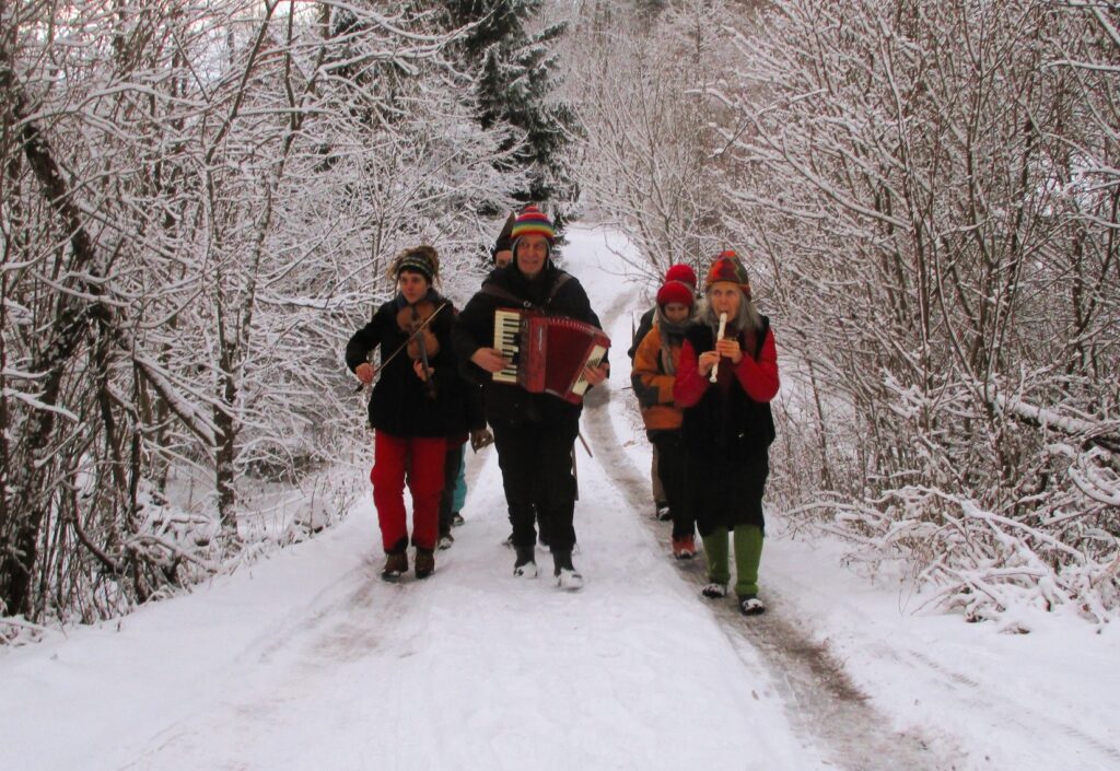 Grupa osób idących w zaspach śnieżnych, grających na instrumentach.