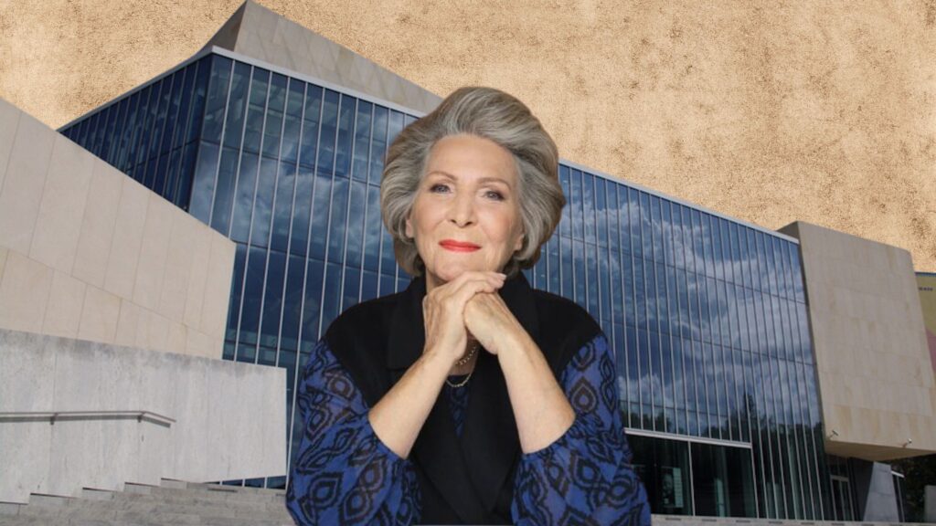 Kobieta z siwymi włosami w eleganckim stroju, z tłem nowoczesnego budynku.