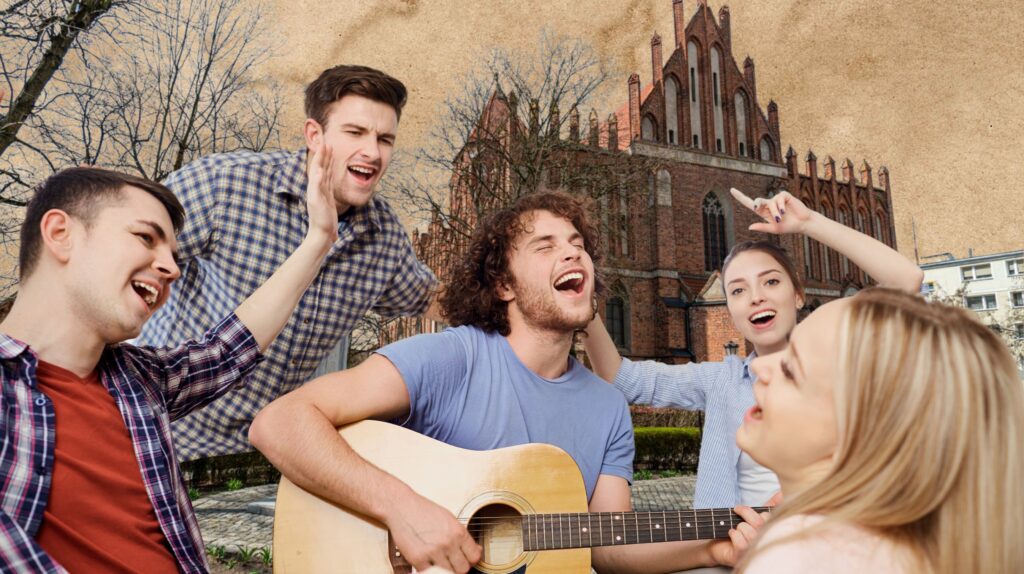 Grupa młodych ludzi śpiewających i grających na gitarze w parku.