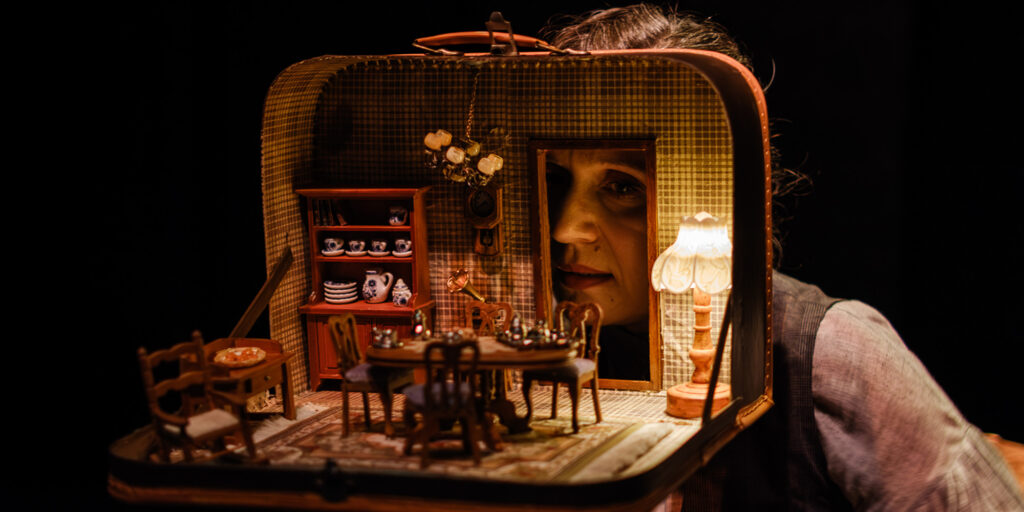 Kobieta patrząca przez miniaturowy pokój w walizce.