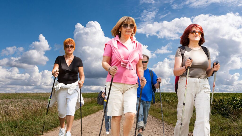 Grupa osób maszerująca z kijkami do nordic walking po polnej drodze.