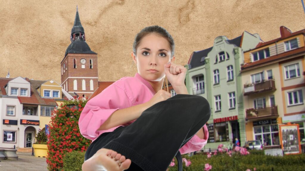 Kobieta w różowej koszuli karate, wykonująca kopnięcie na tle miejskiego krajobrazu.