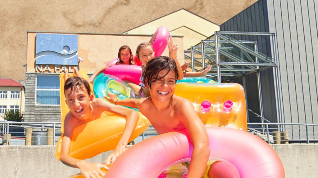 Dzieci bawią się na dmuchanych materacach przy basenie.