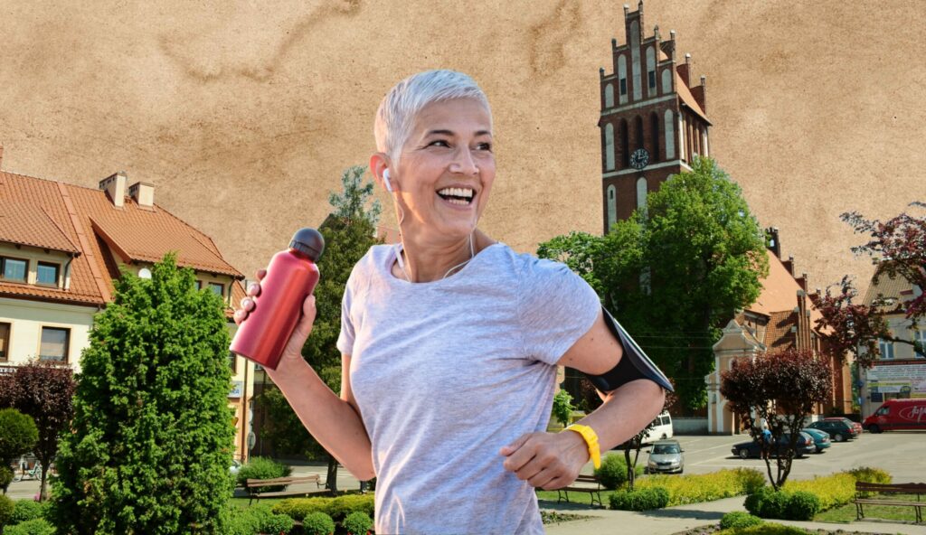 Uśmiechnięta kobieta biegnąca w parku z butelką wody.