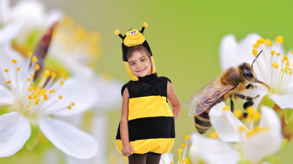 Dziecko w kostiumie pszczoły na tle kwiatów.