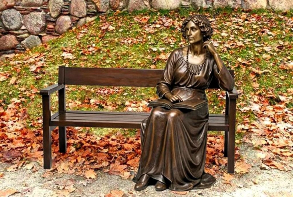 Bronzowa rzeźba kobiety siedzącej na ławce.