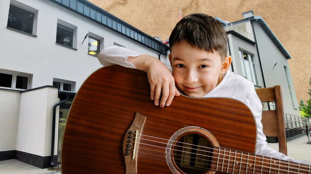 Chłopiec trzymający gitarę w pobliżu budynku.