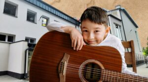 Chłopiec trzymający gitarę w pobliżu budynku.