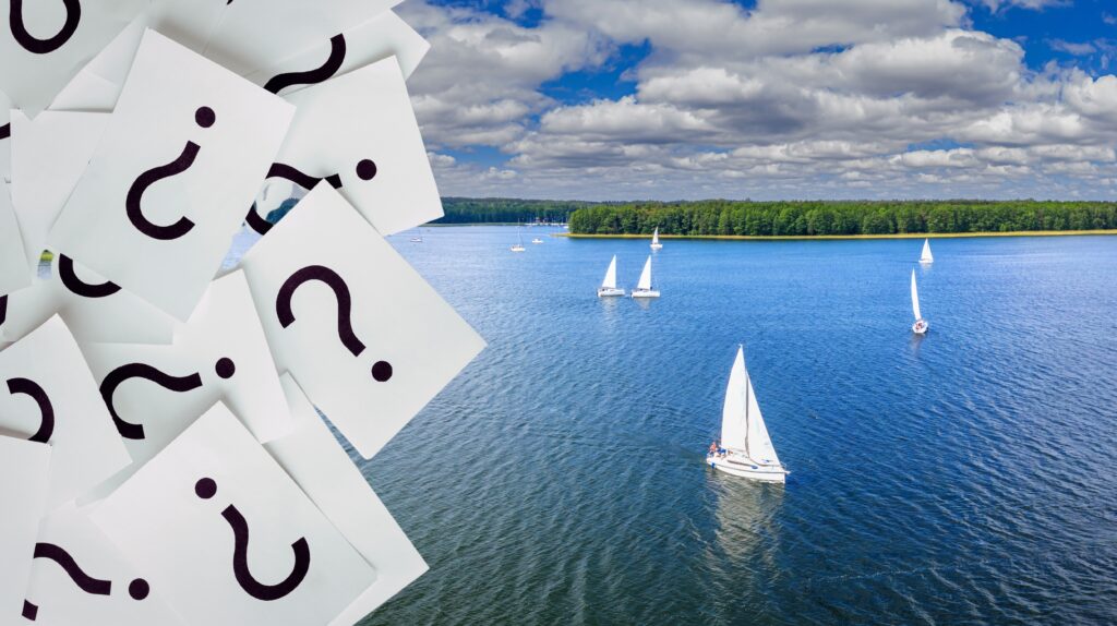 Fragment zdjęcia z żaglówkami na jeziorze i kartkami z pytajnikami.