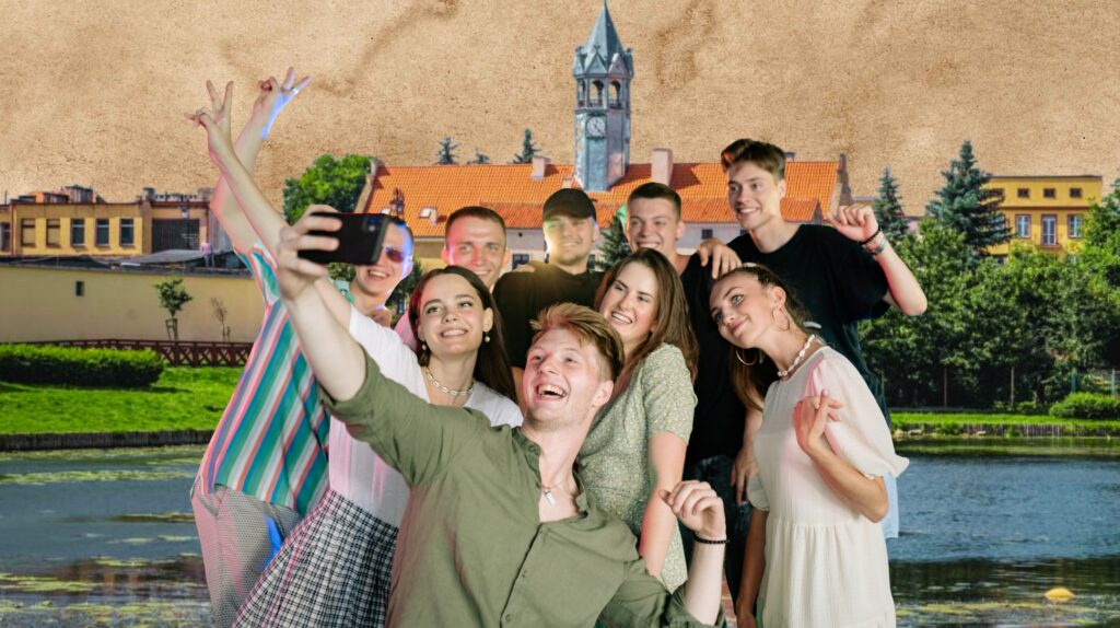 Grupa młodych ludzi robi selfie nad wodą z tłem miejskim.