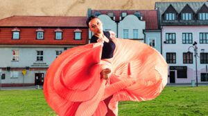 Tancerka w kolorowej spódnicy na tle budynków.