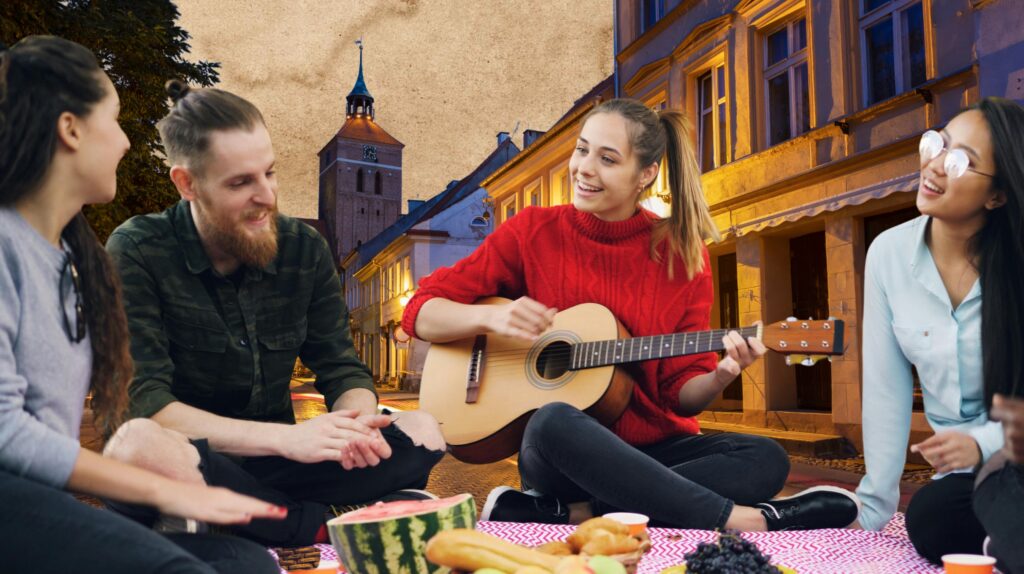 Grupa przyjaciół bawiących się na ulicy, jedna osoba gra na gitarze.