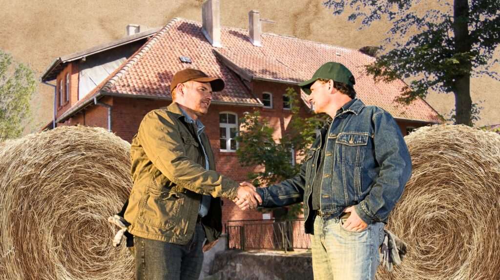 Dwaj mężczyźni podają sobie ręce na tle stodoły.