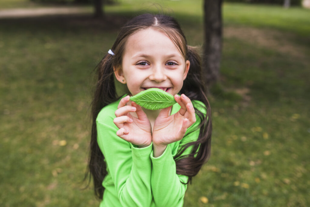 Dziewczynka w zielonej bluzie trzyma liść.