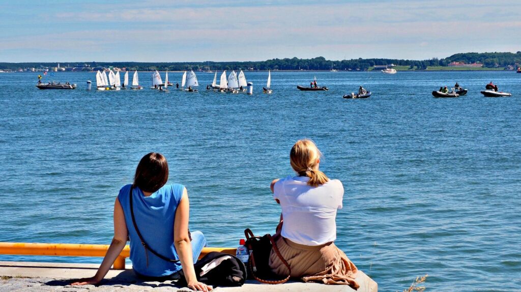 Dwie kobiety siedzą nad wodą, obserwując łodzie