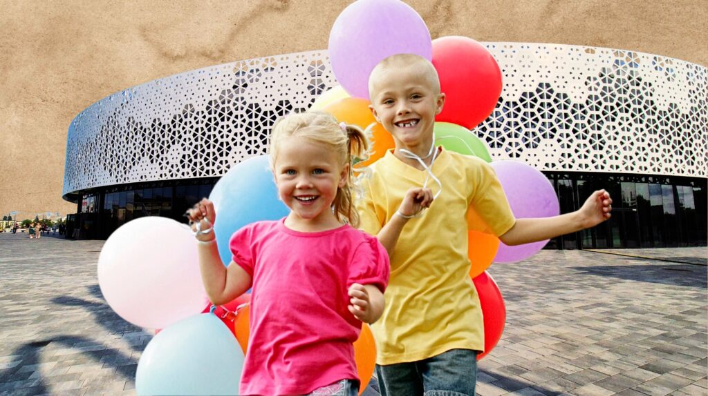 Dzieci bawiące się z balonami na tle nowoczesnego budynku.