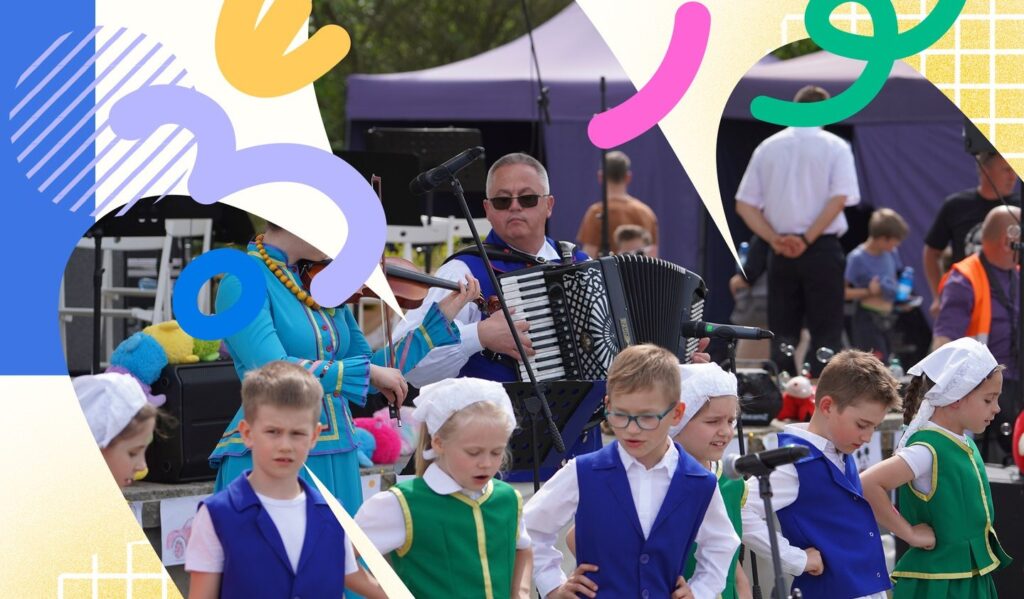 Dzieci w strojach ludowych tańczą na festiwalu, a muzyk gra na akordeonie.