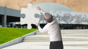 Osoba trzymająca puzzel przed nowoczesnym budynkiem.