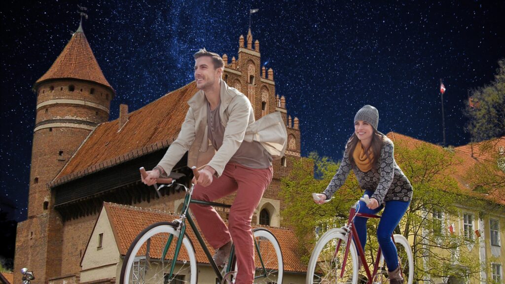Para na rowerach przed zamkiem nocą.