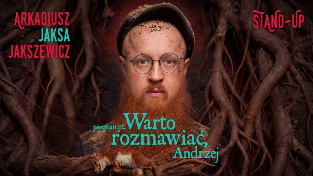 Mężczyzna z długą, rudą brodą, w okrągłych okularach i czapce, otoczony gęstymi korzeniami drzew, z leżącą przed nim sztuczną lub wypchaną wiewiórką i napisem „Warto rozmawiać, Andrzej”