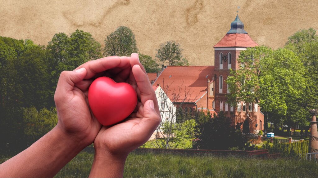 Dwie ręce trzymają czerwone serce na tle budynku.