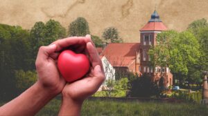 Dwie ręce trzymają czerwone serce na tle budynku.