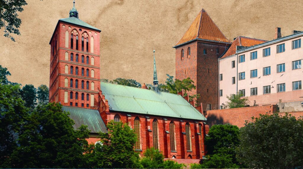 Widok na czerwoną, gotycką katedrę z wieżami i zielonym dachem, otoczoną drzewami.