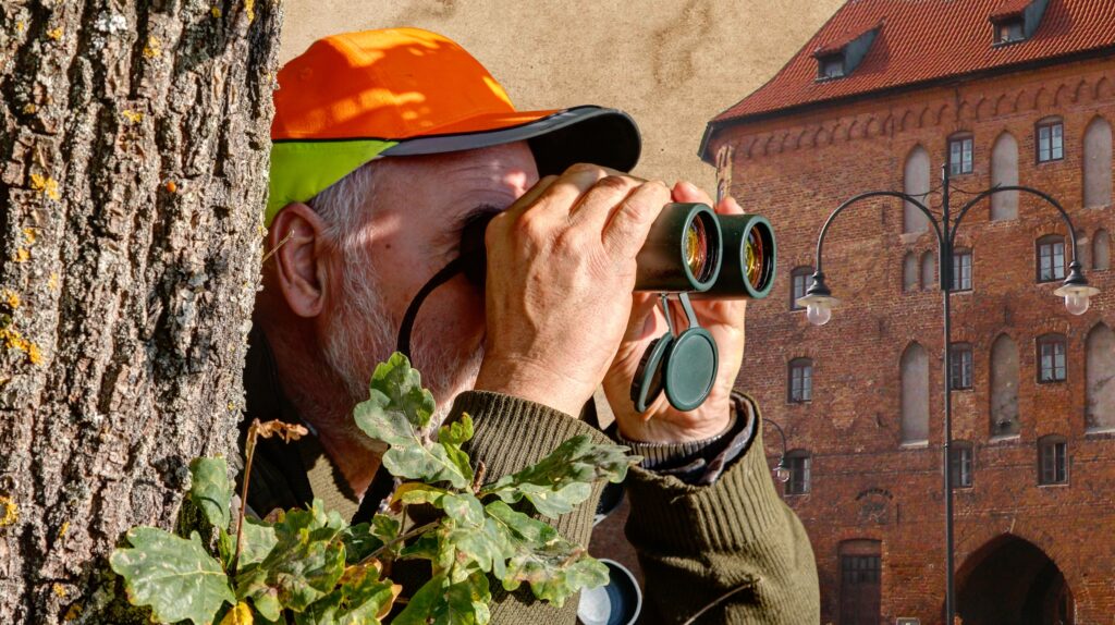 Mężczyzna obserwujący przez lornetkę przy drzewie.